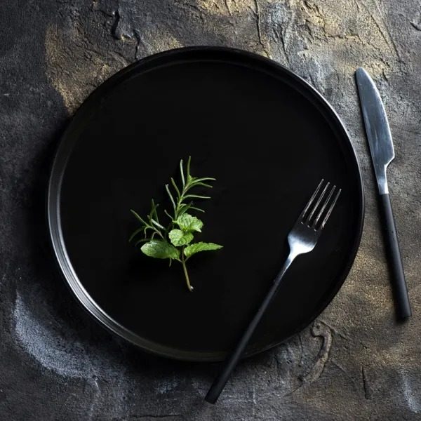 Black plate with a rosemary sprig and black cutlery